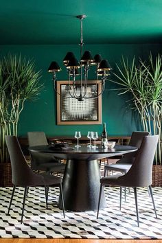 a dining room with green walls, black chairs and a round table surrounded by potted plants