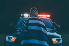 a man in an american flag shirt sitting on the hood of a police car at night