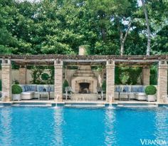 an outdoor fireplace and seating area next to a swimming pool with trees in the background