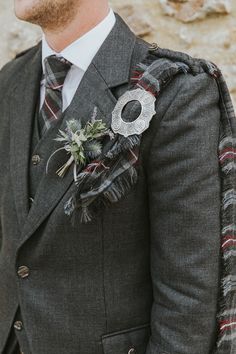 a man in a suit and tie standing next to a stone wall wearing a boutonniere