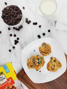 three cookies on a plate with chocolate chips and milk next to it, along with two bags of cookie mix