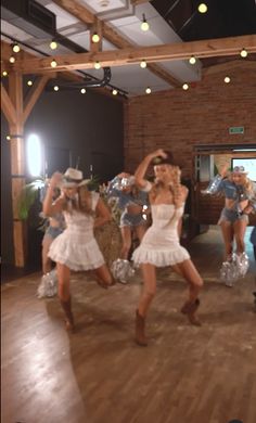 two women in white dresses and cowboy hats dancing on a wooden floor with lights overhead