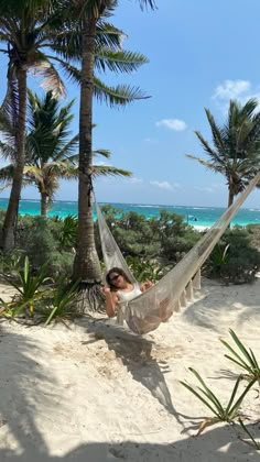 a woman laying in a hammock on the beach with palm trees and ocean in the background