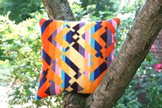 an orange and blue pillow sitting on top of a tree branch