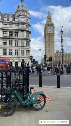 a bicycle parked next to a fence in front of a building with a clock tower