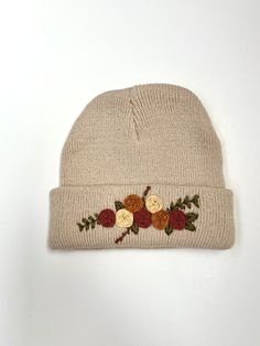 a white beanie with flowers on it sitting on top of a white table next to a pair of scissors