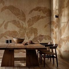 a wooden table sitting in front of a wall with leaves painted on it and two chairs next to it