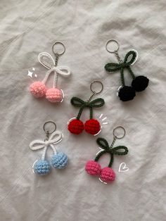 four crocheted cherries with bows and hearts on them sitting on a white sheet