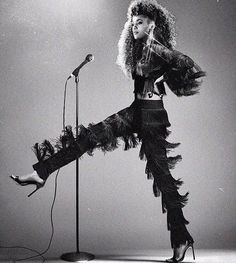 a woman standing in front of a microphone with her legs spread out and wearing feathered pants