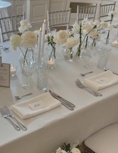 the table is set with silverware and white flowers in vases, candles and napkins