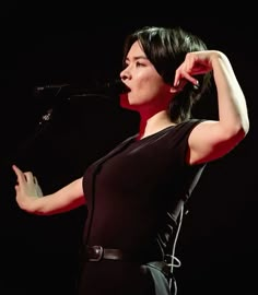 a woman standing in front of a microphone and holding her hand up to her head