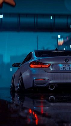 the back end of a silver sports car parked in front of a building at night