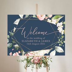 a welcome sign on top of a easel with flowers and greenery around it