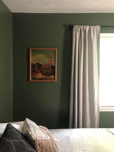 a bedroom with green walls and a painting hanging on the wall next to a bed