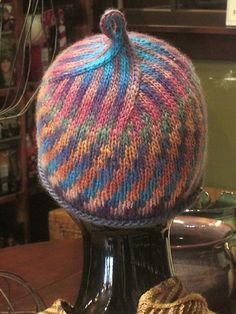 a knitted hat sitting on top of a black vase in front of a shelf