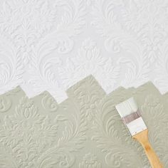 a paintbrush is being used to paint a wall with white and green damask