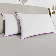 two pillows on top of a bed with white sheets and purple piping in the middle