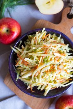 an apple and carrot slaw salad in a bowl next to two apples on a cutting board