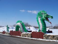 two large green dragon statues sitting on the side of a road next to snow covered ground