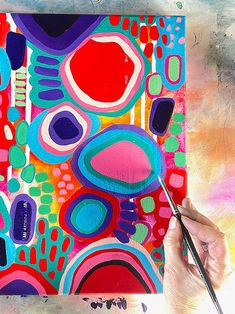 a person holding a paintbrush in front of a colorful painting with circles and dots on it