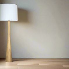 a floor lamp with a white shade on it in front of a wall and wooden floor