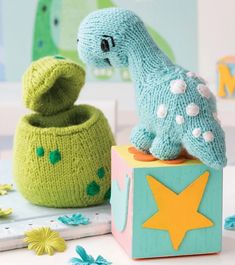 a knitted toy dinosaur sitting on top of a wooden block next to another toy