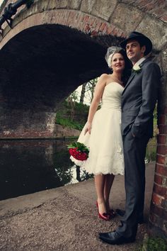 a bride and groom standing next to each other in front of a stone bridge over water