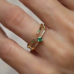 a woman's hand with two gold rings and emeralds on it, one is holding the other