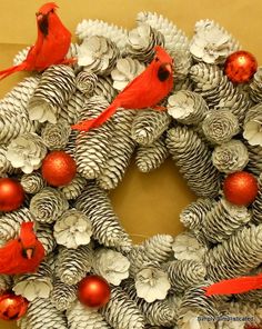 a christmas wreath with red birds and pine cones on the front, hanging from a wall