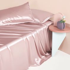 a bed with pink sheets and pillows on top of it next to a nightstand table