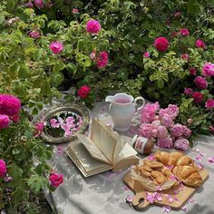 an open book on a table surrounded by pink flowers and other items in front of it