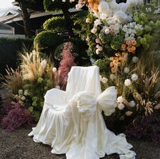 a white chair sitting on top of a lush green field next to tall grass and flowers