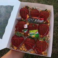 someone is holding a box with strawberries and other food items in it on the grass