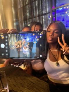 a woman holding up a cell phone to take a selfie with friends in the background