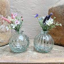 three glass vases with flowers in them sitting on a stone ledge next to rocks