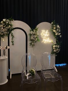 two clear chairs sitting next to each other in front of a wall with flowers on it