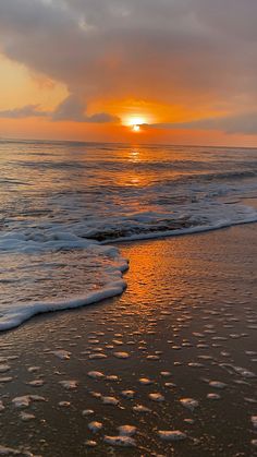 the sun is setting over the ocean with waves coming in to shore and footprints on the sand