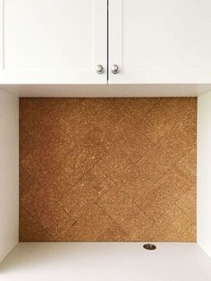 a kitchen with white cabinets and cork backsplash in the corner, under an overhead cabinet door