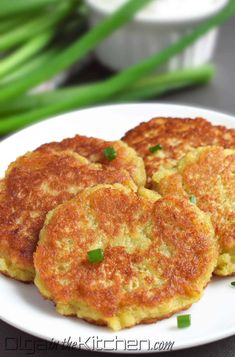 three crab cakes on a white plate with green onions