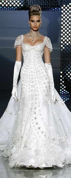 a model walks down the runway in an embellished white gown and matching gloves