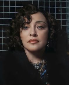 a woman with curly hair and blue eyes stares into the distance while standing in front of a wire fence