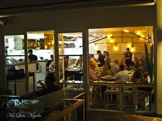 a group of people sitting at tables in front of a restaurant with lots of windows