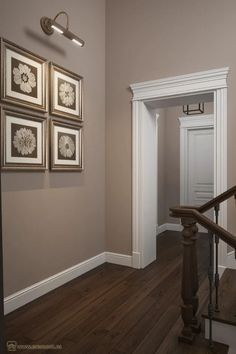 an empty hallway with framed pictures on the wall and wooden stairs leading to another room