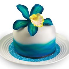 there is a blue and white cake with a flower on the top, sitting on a plate