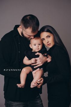 a man and woman holding a baby while posing for a photo in front of a gray background