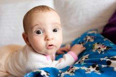 a baby laying on top of a bed covered in a blue and white blanket looking at the camera