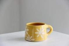 a yellow mug with white flowers on it sitting on top of a table next to a wall