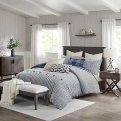 a bedroom with gray walls, white curtains and blue bedding on the bed is shown