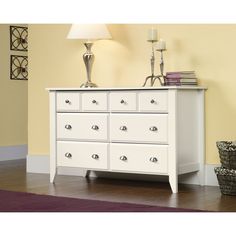 a white dresser sitting in a room next to a lamp