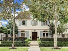 a white house with hedges and trees in the front yard